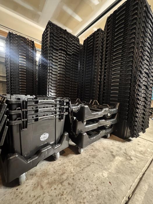Dollies staged in front of floor-to-ceiling stacks of black moving totes