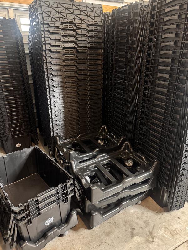 Warehouse stacks of collapsed black moving totes next to plastic dollies